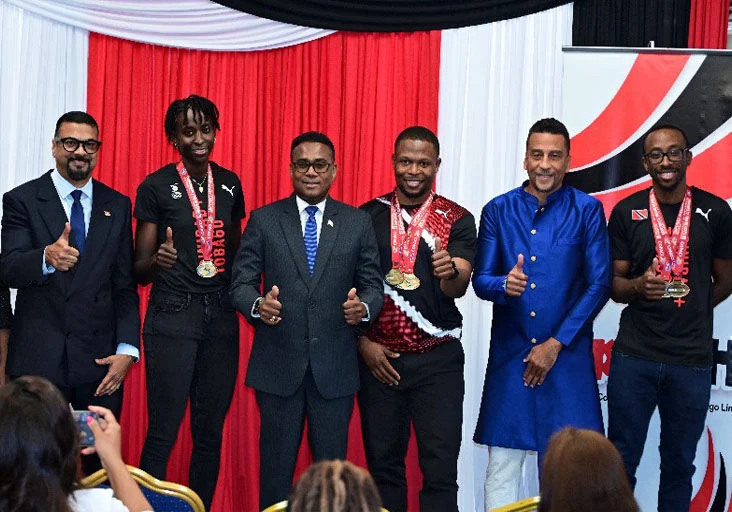THUMBS UP: Parliamentary Secretary in the Ministry of Tertiary Education and Skills Training, Hansen Narinesingh, left, Minister of Sport and Youth Affairs, Phillip Watts, third from left, and David Nakhid, Parliamentary Secretary in MSYA, second from right, join Team TTO cyclists Teniel Campbell, second from left, Nicholas Paul, fourth from left, and Akil Campbell, right, during an official welcome reception held in the team’s honour at the Hasely Crawford Stadium, Mucurapo, yesterday. —Photo: JERMAINE CRUICKSHANK (Image obtained at trinidadexpress.com)